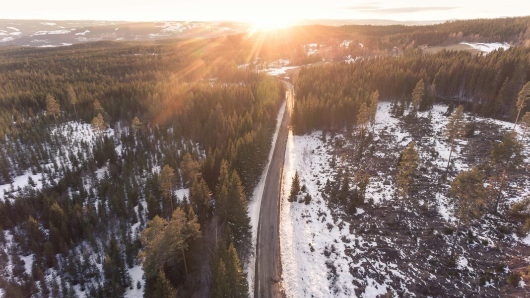 norwegia Zapierający dech w piersiach widok z lotu ptaka na zaśnieżoną leśną drogę o wschodzie słońca w Norwegii, podkreślający spokojne piękno zimy.
