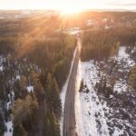 Zapierający dech w piersiach widok z lotu ptaka na zaśnieżoną leśną drogę o wschodzie słońca w Norwegii, podkreślający spokojne piękno zimy.