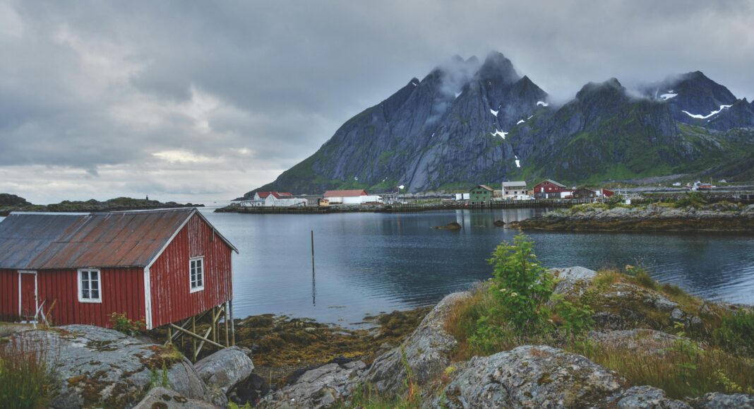 norwegia Malownicza nordycka wioska z drewnianymi chatami nad fiordem, otoczona ośnieżonymi górami.