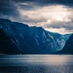 Ujęcie dramatycznego norweskiego fiordu z wysokimi klifami i spokojną wodą odbijającą nastrojowe niebo.