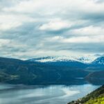 Norweski model pracy i work-life balance Zapierający dech w piersiach krajobraz ośnieżonych norweskich gór i spokojnego jeziora odbijającego zachmurzone niebo.