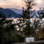 Krótkie wyjazdy do Włoch – co zobaczyć w dwa dni? Spokojny widok na krajobraz z dwoma kubkami do kawy na drewnianej poręczy o zachodzie słońca.