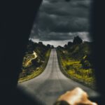 Jak zorganizować weekendowy wyjazd do Hiszpanii? Nastrojowa jazda otwartą drogą z ciemnymi chmurami nad głową, ukazująca poczucie przygody i samotności.