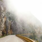 Krótkie wyjazdy do Belgii – co zobaczyć w dwa dni? Kręta górska droga pod mglistymi klifami oferuje tajemnicze wrażenia z podróży.