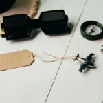 Jak zaplanować krótki wyjazd do Paryża? Płaski układ niezbędnych artykułów podróżnych, w tym modelu samolotu, okularów przeciwsłonecznych, kompasu i kapelusza na stole.