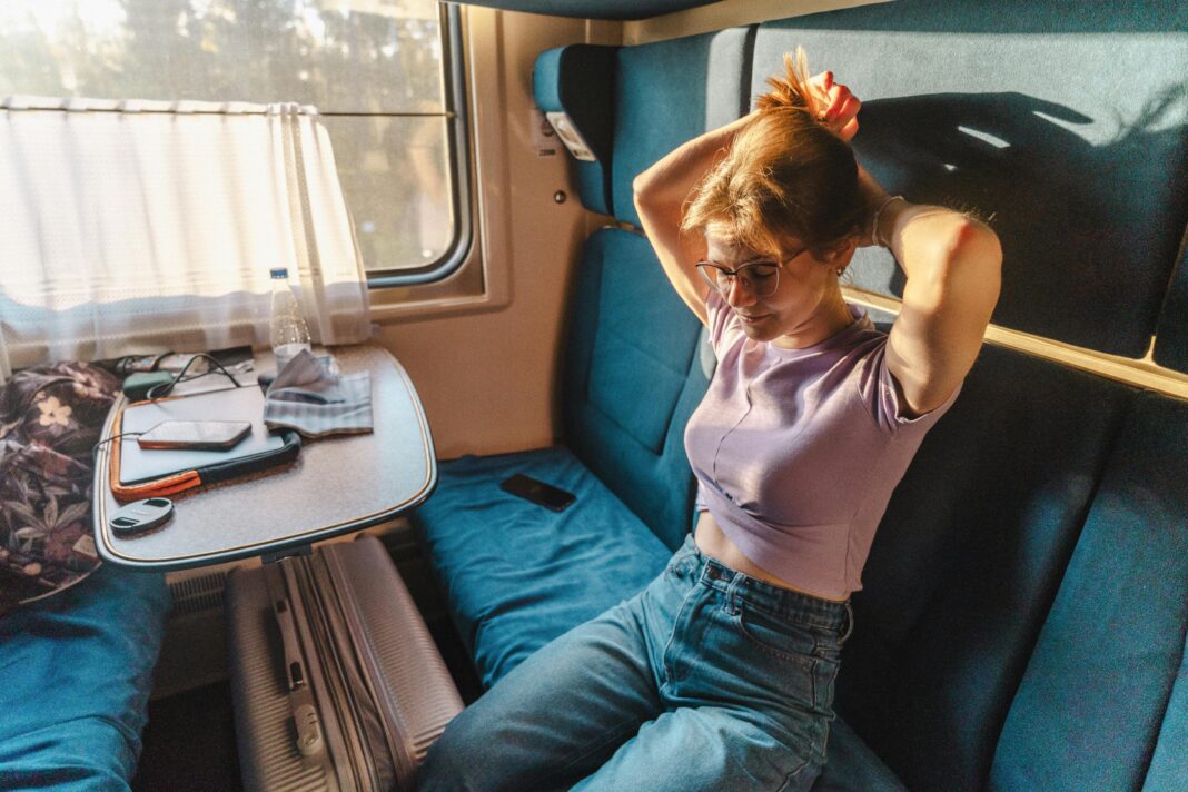 Młoda kobieta w przedziale pociągu wiążąca włosy w popołudniowym słońcu.