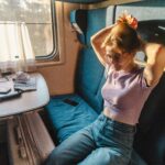 Młoda kobieta w przedziale pociągu wiążąca włosy w popołudniowym słońcu.