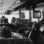 Monochromatyczny widok wnętrza autobusu pełnego siedzących pasażerów podczas podróży.