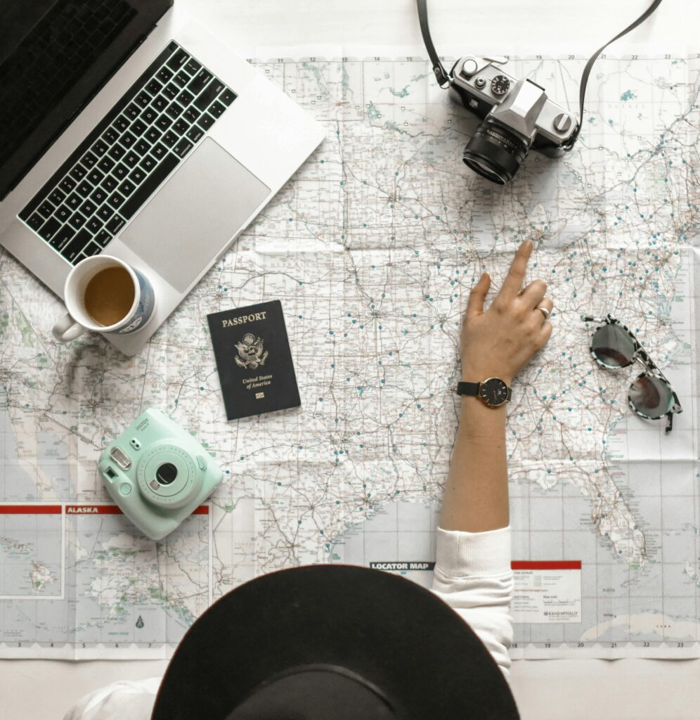 Ręka na mapie z aparatem, paszportem, laptopem i kawą, idealna do inspiracji w zakresie planowania podróży.