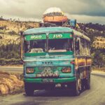 Kolorowy zabytkowy autobus podróżujący malowniczą wiejską drogą pod pochmurnym niebem.