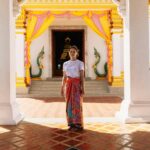 Kobieta stoi przy tętniącym życiem wejściu do świątyni w Krabi w Tajlandii, ozdobionym kolorowymi draperiami i architekturą.