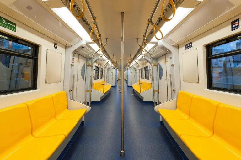 Wnętrze nowoczesnego wagonu metra z jasnożółtymi siedzeniami i czystym designem, podkreślającym transport publiczny.