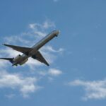 Samolot pasażerski lecący wysoko na czystym, błękitnym niebie z rozproszonymi chmurami.