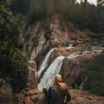 Kobieta siedzi na klifie w Silver Bay w stanie Minnesota i podziwia zapierający dech w piersiach wodospad otoczony bujnymi lasami.
