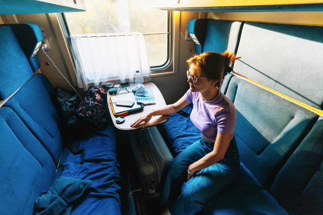 Młoda kobieta siedząca w ciągu dnia w przedziale prywatnego pociągu i ciesząca się podróżą.