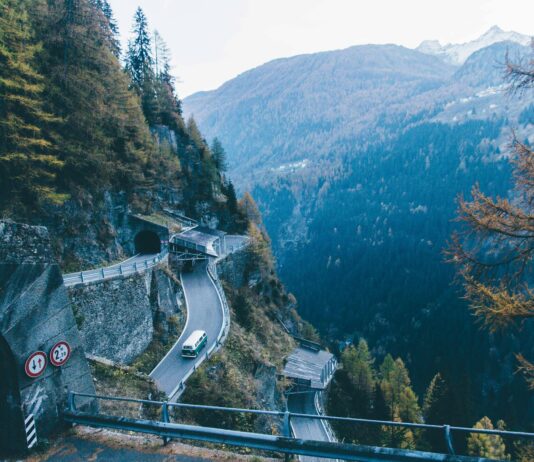 Zapierający dech w piersiach widok na górską drogę z tunelem i furgonetką jadącą przez las sosnowy pod dużym kątem.