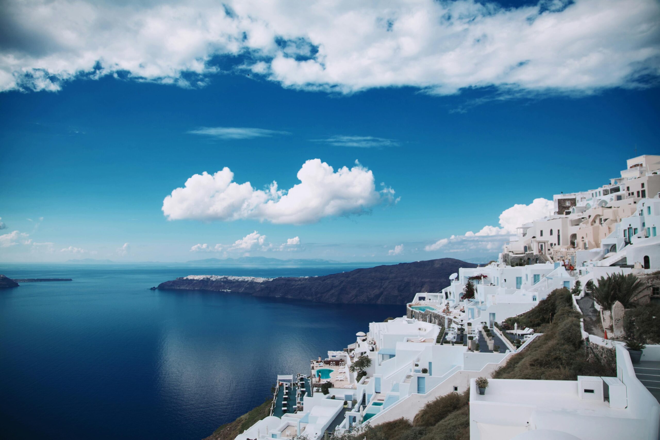 Zapierający dech w piersiach panoramiczny widok na bieloną architekturę Santorini na tle ciemnoniebieskiego morza.