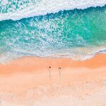 Oszałamiające zdjęcia lotnicze piaszczystej plaży z turkusowymi falami oceanu, ukazujące naturalne piękno wybrzeża.