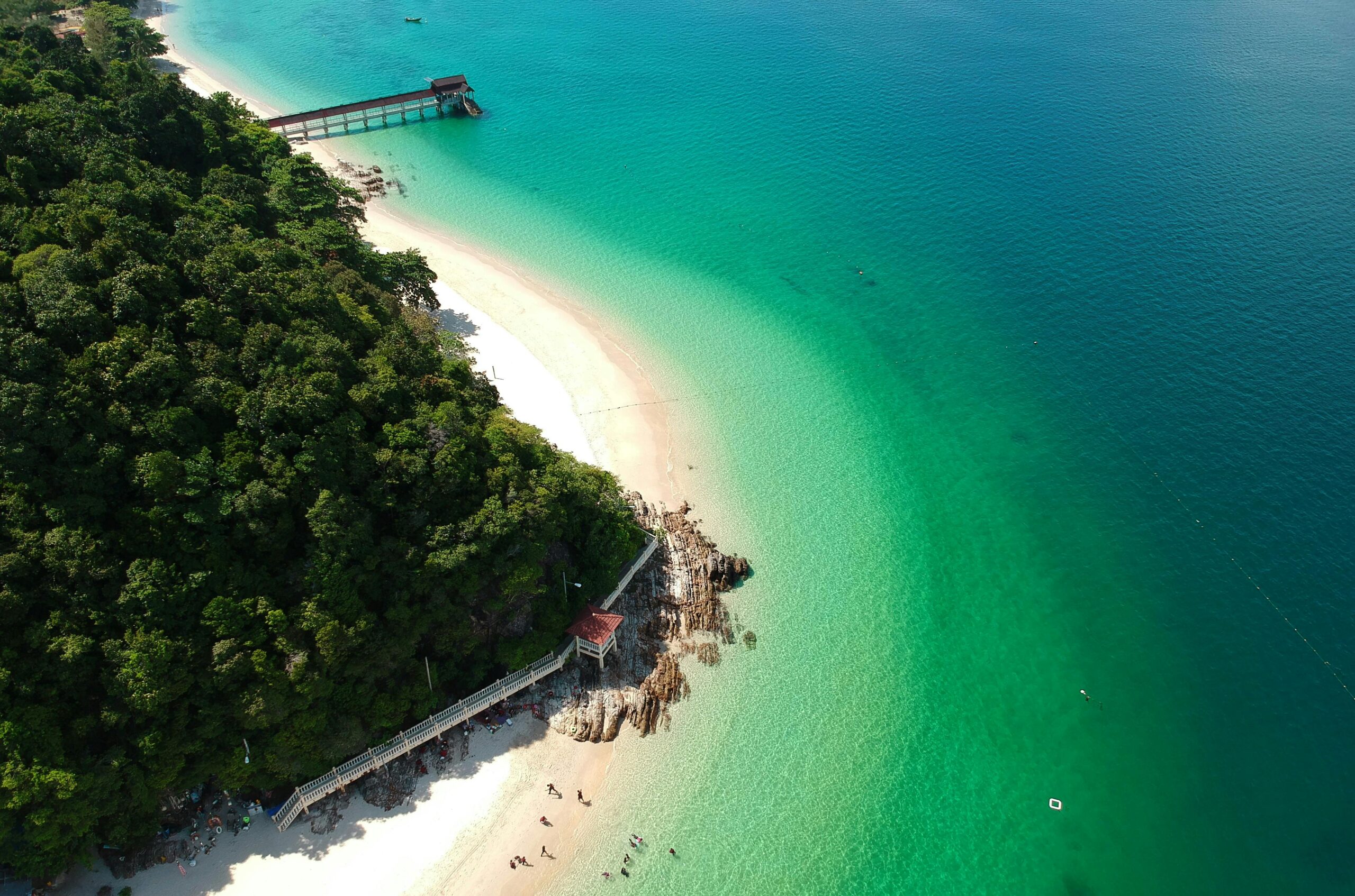 Oszałamiający widok z lotu ptaka na tropikalną plażę z bujnymi drzewami, turkusową wodą i białym piaskiem, idealny do wypoczynku i turystyki.