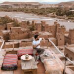 Fakty i mity o jet lagu Mężczyzna pijący herbatę na tarasie na dachu z widokiem na Ait Benhaddou w Maroku.