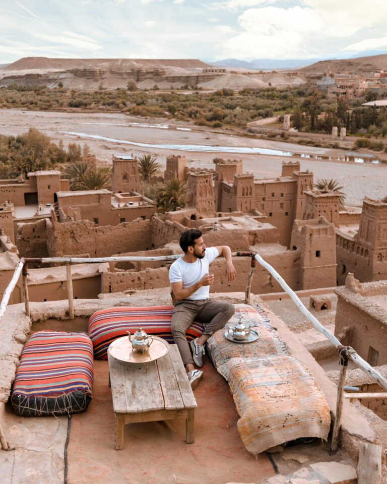 Mężczyzna pijący herbatę na tarasie na dachu z widokiem na Ait Benhaddou w Maroku.