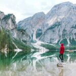 Osoba stojąca nad malowniczym jeziorem Braies z majestatycznymi górami Dolomitów odbitymi w wodzie.