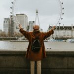 Fakty i mity o podróżach do egzotycznych krajów Osoba z podniesionymi rękami oglądająca London Eye przez Tamizę jesienią.