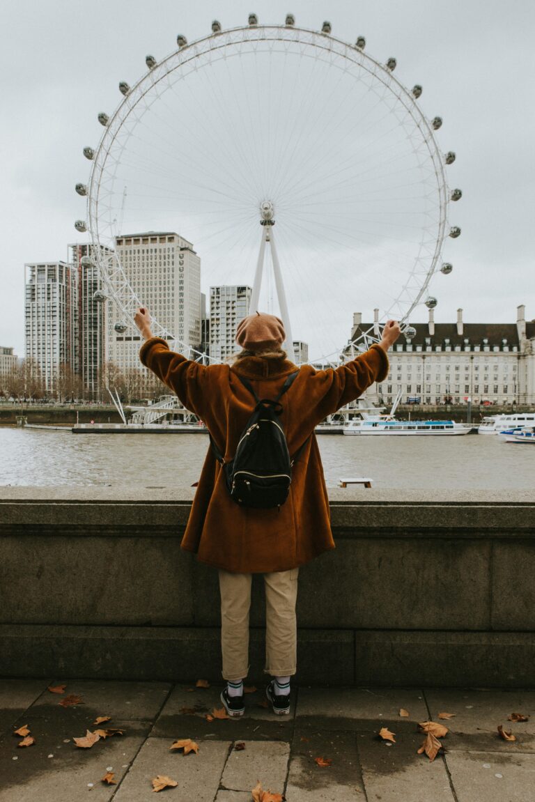 Osoba z podniesionymi rękami oglądająca London Eye przez Tamizę jesienią.