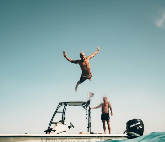 Dwóch mężczyzn przeżywa słoneczną przygodę, wskakując z łodzi do morza Abu Zabi.