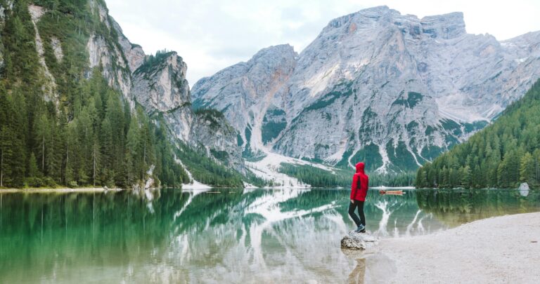 Osoba stojąca nad malowniczym jeziorem Braies z majestatycznymi górami Dolomitów odbitymi w wodzie.