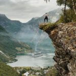 Fakty i mity o kartach SIM dla podróżników Osoba cieszy się zapierającym dech w piersiach widokiem z klifu nad fiordem Geiranger w Norwegii, z czystym niebem i statkiem wycieczkowym poniżej.