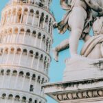 Krzywa Wieża w Pizie obok ozdobnego posągu cheruba na tle czystego, błękitnego nieba.