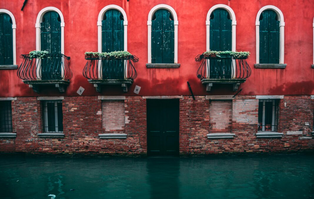 wlochy Elegancki wenecki budynek nad kanałem z ozdobnymi balkonami i jaskrawą czerwoną fasadą.