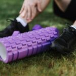 Czarne buty sportowe i fioletowy wałek do ćwiczeń na trawie