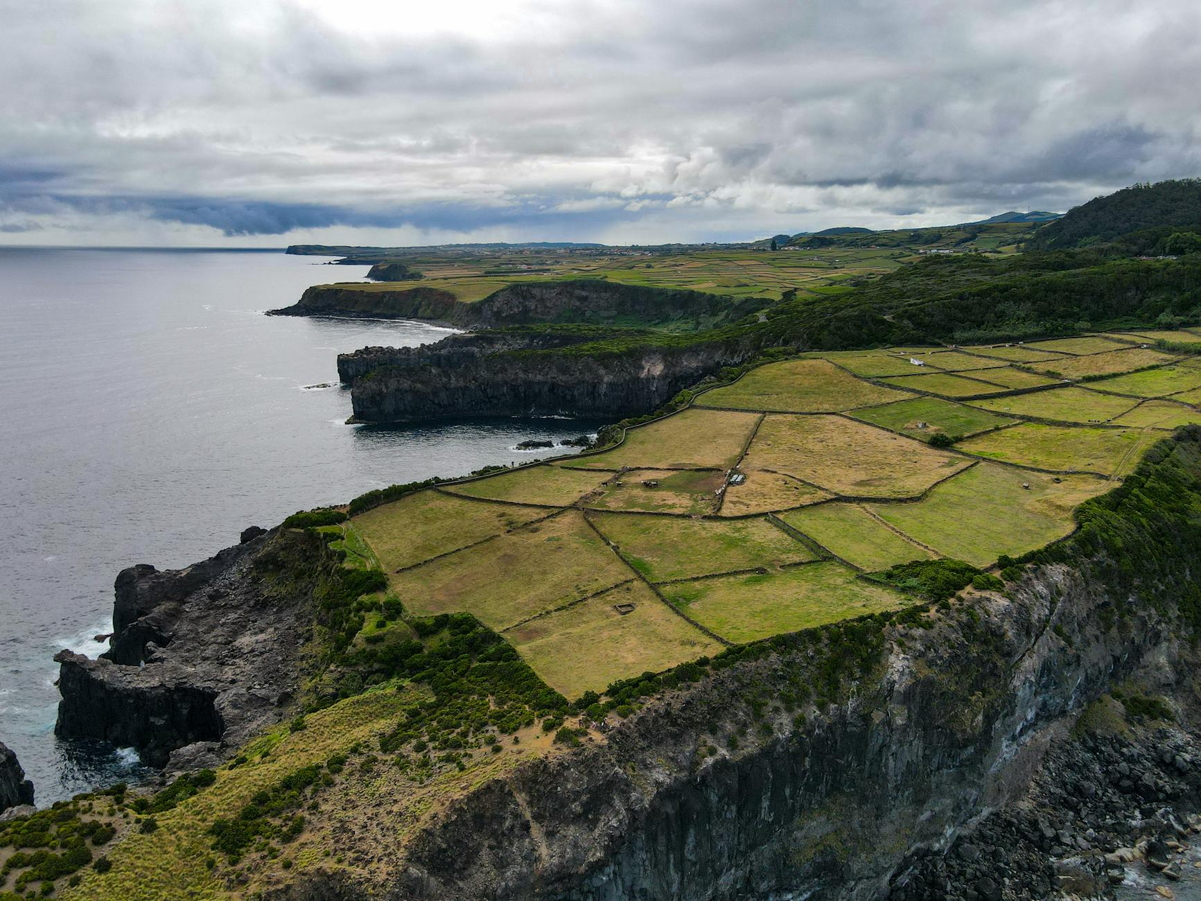 Tarasowe pola uprawne nad klifowym wybrzeżem Azorów pod chmurnym niebem