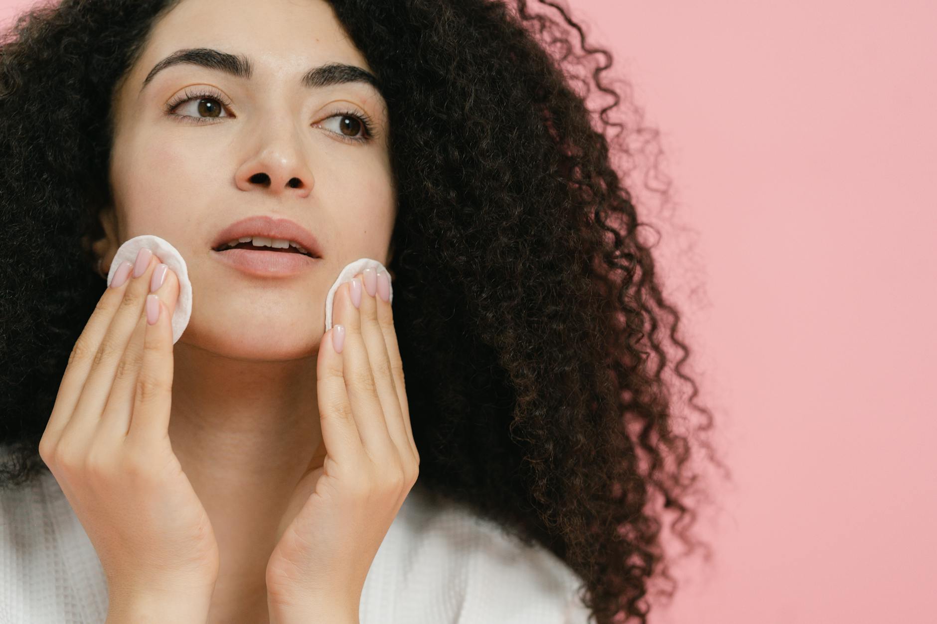 Kobieta oczyszcza twarz płatkami kosmetycznymi na różowym tle