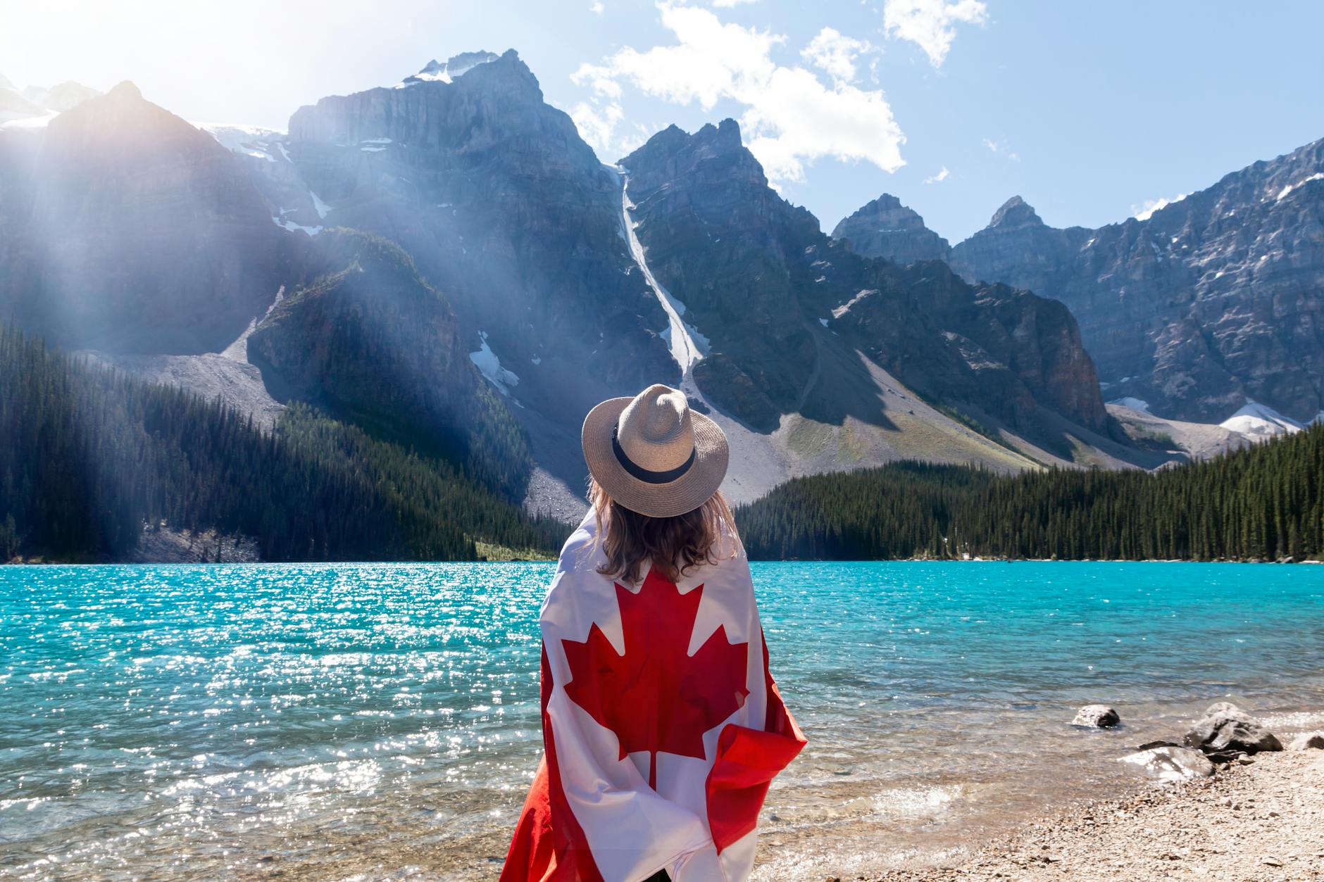 Osoba w kapeluszu owinięta flagą Kanady patrzy na jezioro Moraine Lake