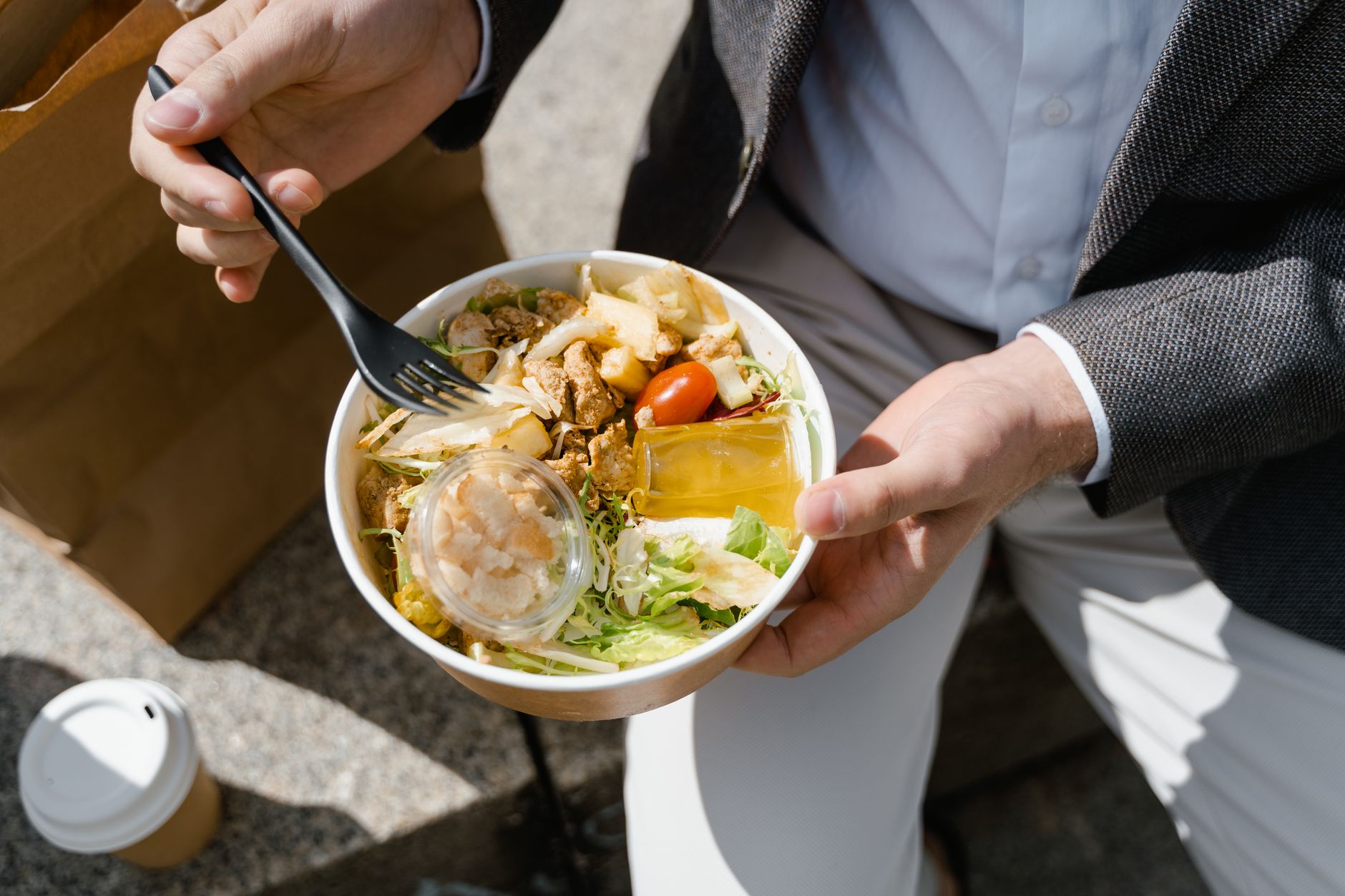 Mężczyzna je świeżą sałatkę i pije kawę na przerwie na lunch