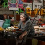 Starsza Tajka smaży dania street food na zatłoczonym targu w Bangkoku