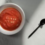 Talerz pomidorowej z napisem Lunch Time i czarna łyżka na marmurze